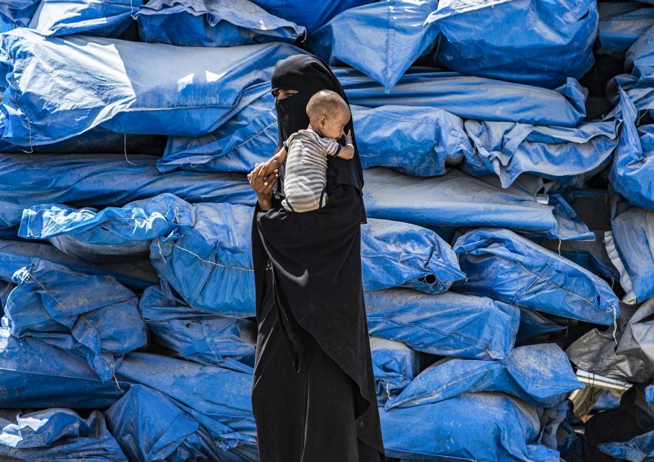 Una mujer usando un nicab camina con un bebé en el campo para desplazados en el noreste de Siria Una mujer usando un nicab camina con un bebé en el campo para desplazados en el noreste de Siria