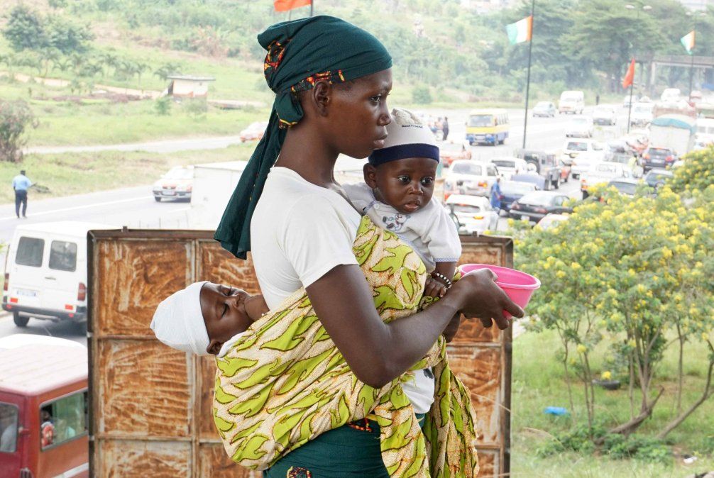Una mujer con sus dos hijos pide comida en Costa de Marfil