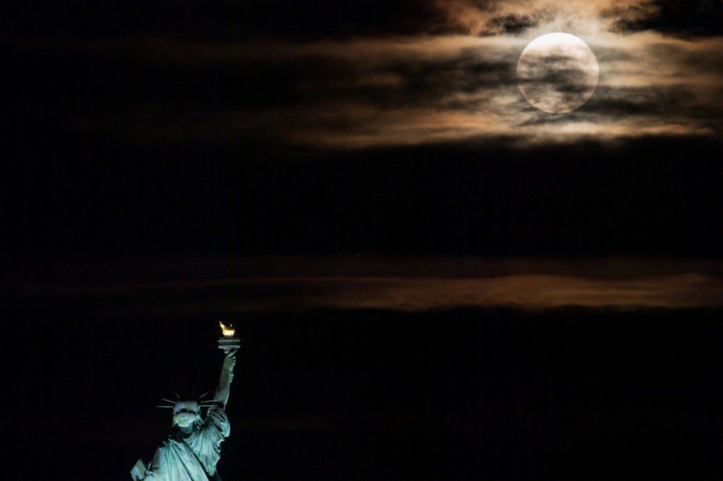 La luna llena se eleva detrás de la Estatua de la Libertad en la ciudad de Nueva York. La luna llena de junio a menudo se conoce como la luna de la fresa porque cae durante la temporada de cosecha de fresas en el noreste de los EE. UU. La luna llena se eleva detrás de la Estatua de la Libertad en la ciudad de Nueva York. La luna llena de junio a menudo se conoce como la luna de la fresa porque cae durante la temporada de cosecha de fresas en el noreste de los EE. UU.