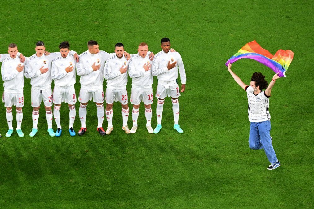 Una persona que agita la bandera del arco iris corre en el campo mientras los jugadores de Hungría se alinean para los himnos nacionales del partido de fútbol del Grupo F de la UEFA EURO 2020 entre Alemania y Hungría. Una persona que agita la bandera del arco iris corre en el campo mientras los jugadores de Hungría se alinean para los himnos nacionales del partido de fútbol del Grupo F de la UEFA EURO 2020 entre Alemania y Hungría.