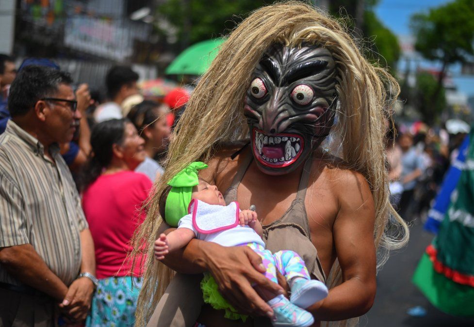 Un hombre con una máscara de un personaje mitológico sosteniendo un bebé participa de un desfile en el Festival Divino Salvador del Mundo, en San Salvador