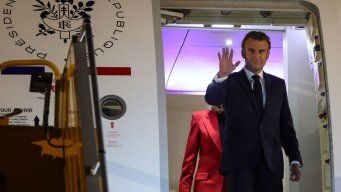 Macron al bajar del avión junto a su esposa, en ese momento detrás, luego al costado. Foto: AFP