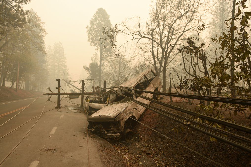 Una columna de energía eléctrica caída y un auto completamente quemado a un lado de la calle en Paradise, California.