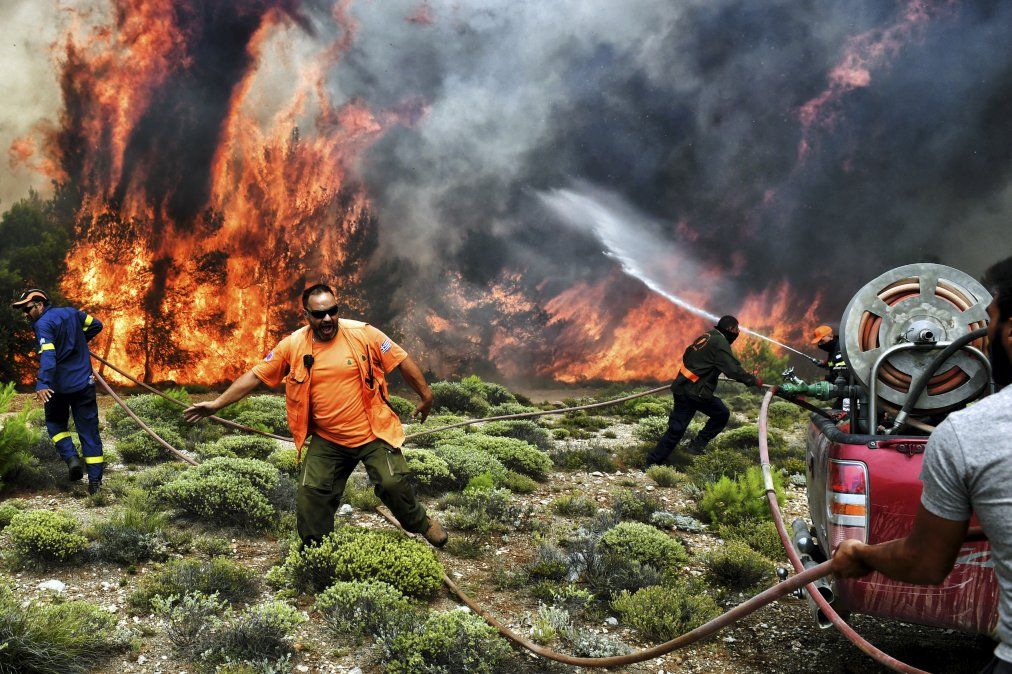 Bomberos y voluntarios intentan extinguir las llamas durante un incendio forestal en la aldea de Kineta, cerca de Atenas
