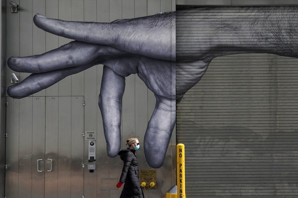 Una mujer con tapabocas pasa frente a un mural de una mano sobre un edificio en Nueva York