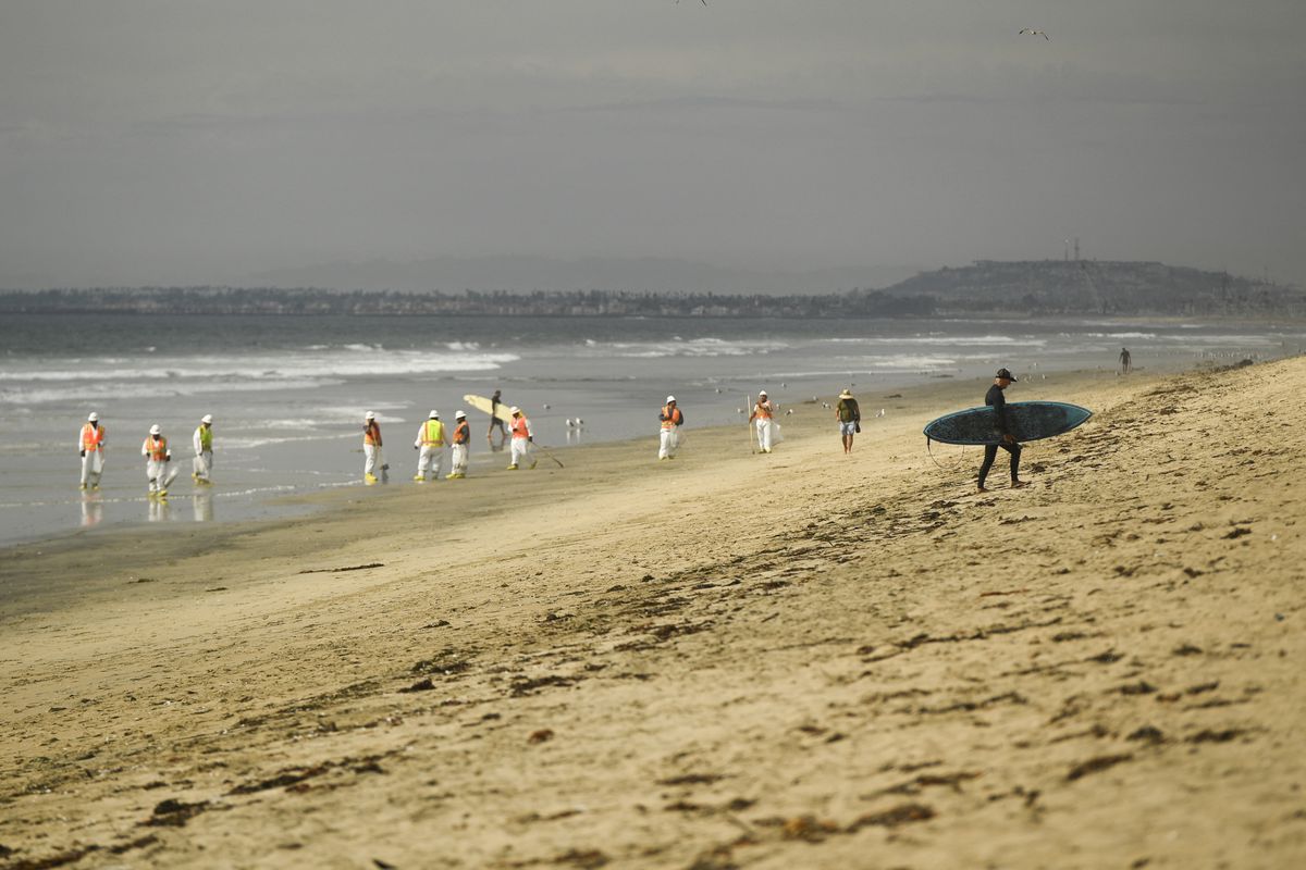 Un surfista camina por la playa mientras los equipos de respuesta ambiental limpian la playa después de un derrame de petróleo en el Océano Pacífico en Huntington Beach, California, Estados Unidos.&nbsp;