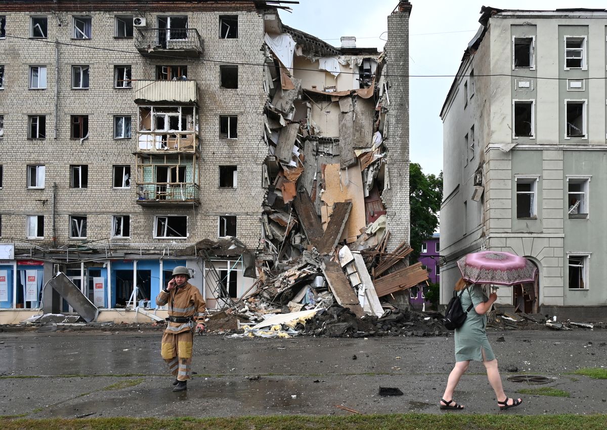 Un residente local pasa junto a un rescatista ucraniano que trabaja fuera de un edificio parcialmente destruido después de un ataque con misiles rusos en Kharkiv el 11 de julio de 2022, en medio de la invasión militar de Rusia lanzada contra Ucrania. Foto: AFP