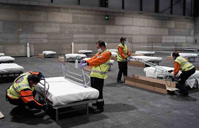 Trabajadores colocan camas de un hospital temporal para pacientes con coronavirus en el centro de exposiciones Ifema en Madrid