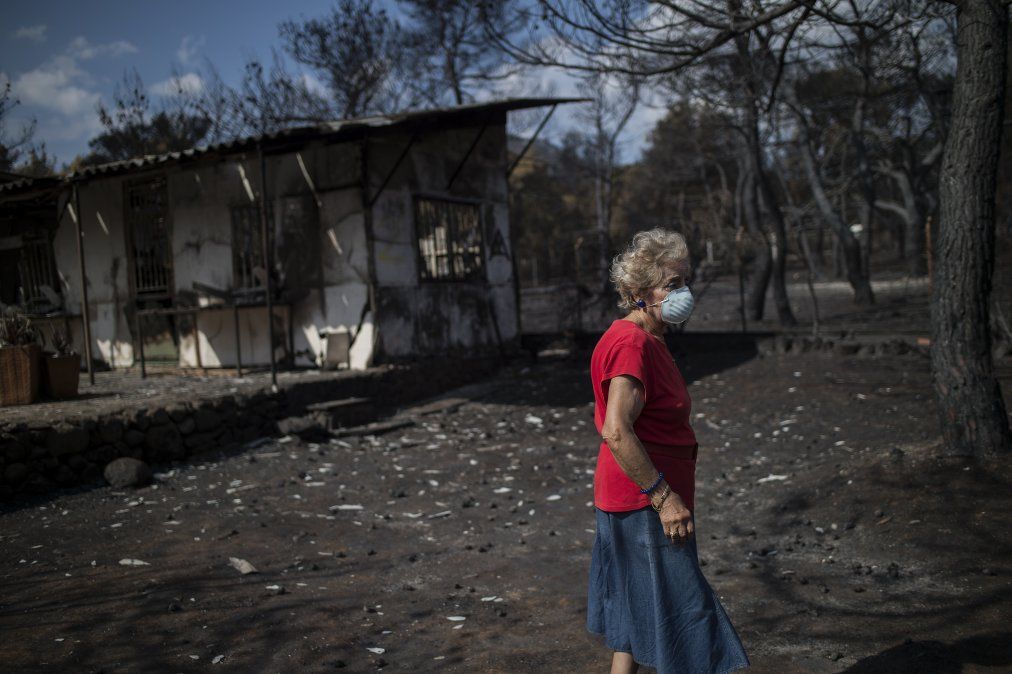 Una mujer usa una máscara frente a su casa incencendiada en Grecia
