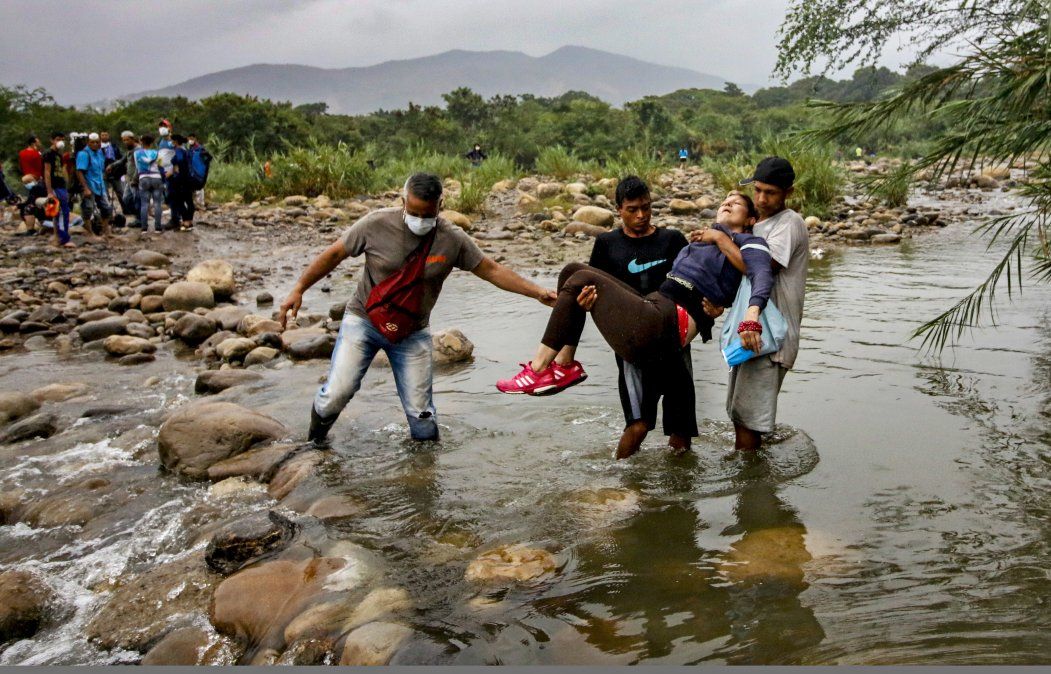Ciudadanos venezolanos con mascarillas protectoras para prevenir la propagaci&oacute;n del coronavirus llevan a una mujer inconsciente mientras intentan ingresar a Colombia