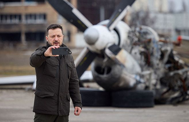 El presidente de Ucrania Volodomir Zelenski se saca una foto con restos de un avión caído, en el segundo aniversario de la invasión rusa a su país. Foto: AFP.