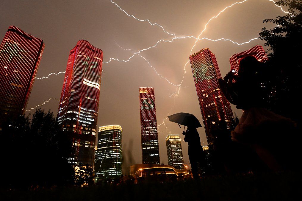 Un rayo cruza el cielo mientras la gente mira los edificios que muestran un espectáculo de luces en la víspera del centenario del Partido Comunista de China en Beijing