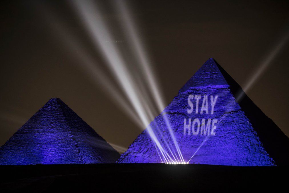 Grandes Pir&aacute;mides iluminadas con luz azul y el mensaje Qu&eacute;dese en casa en la meseta de Giza, en las afueras de Egipto.