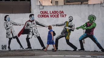 En esta foto de archivo tomada el 12 de junio de 2020, una mujer pasa junto a un mural que representa al presidente brasileño Jair Bolsonaro y una figura que representa al nuevo coronavirus COVID-19 tirando de una cuerda contra los trabajadores de la salud con la pregunta ¿De qué lado de la cuerda estás? En Sao Paulo, Brasil, se confirmó el tercer caso de la nueva variante COVID-19, omicron, en un viajero proveniente de Etiopía