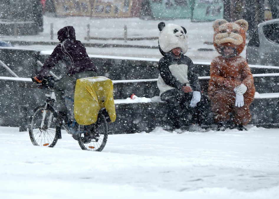 Un hombre en bicileta pasa al lado de dos personas disfrazadas de animales durante una fuerte nevada en Kiev, la primera del otoño.