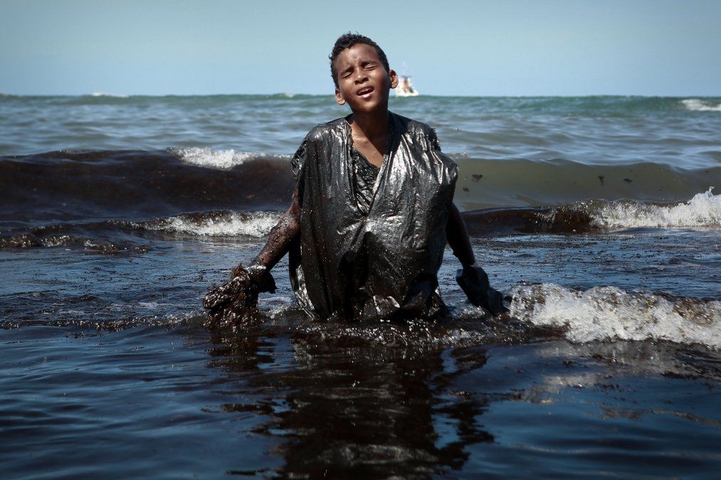 Un niño camina fuera del mar y sale cubierto de petróleo derramado en la playa de Itapuama en el estado de Pernambuco, Brasil.&nbsp;