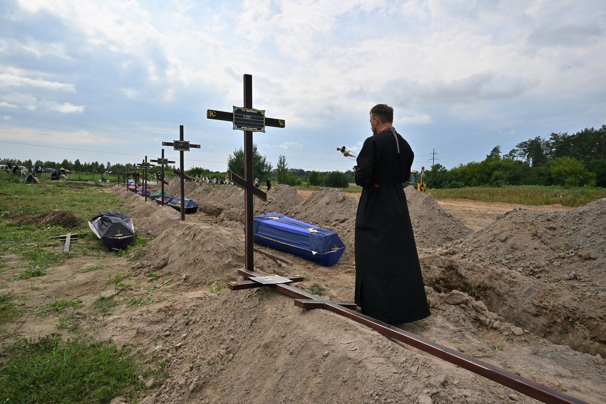 El sacerdote ortodoxo Andriy Golovin recita una oración en las tumbas de civiles no identificados durante un funeral en un cementerio local en la ciudad de Bucha, región de Kiev, Ucrania, el 11 de agosto de 2022. Foto: AFP