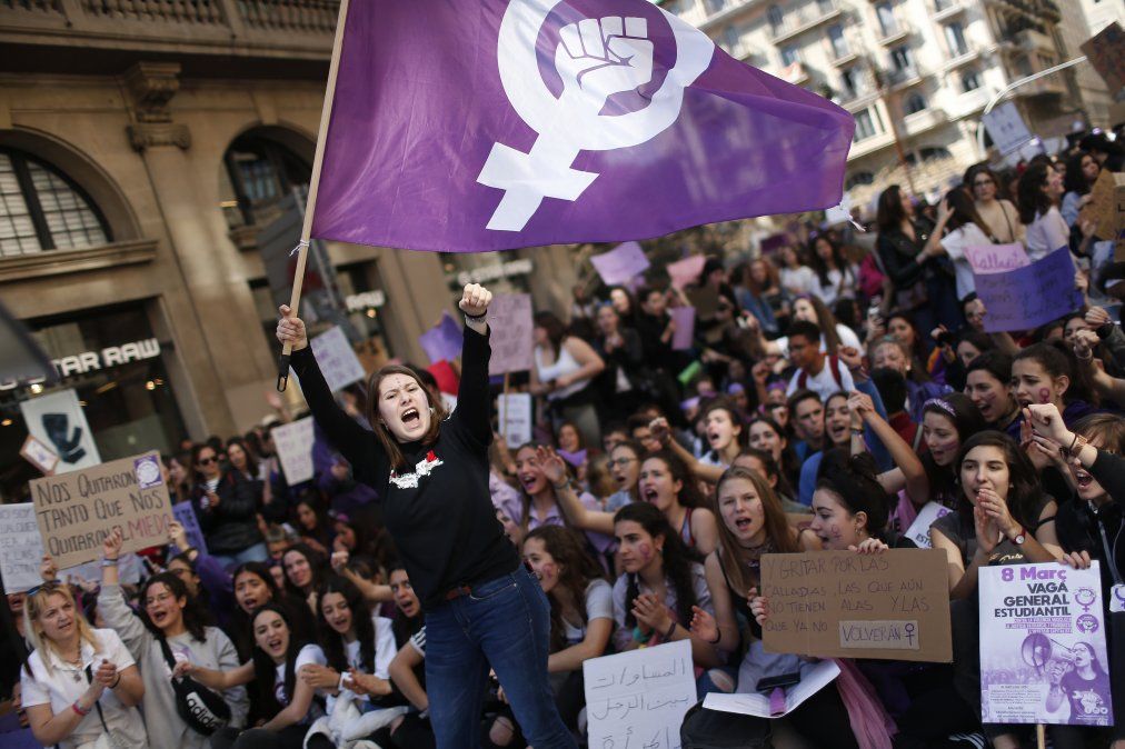 En España una mujer flamea una bandera feminista mientras los estudiantes gritan slogans por el Día Internacional de la Mujer.