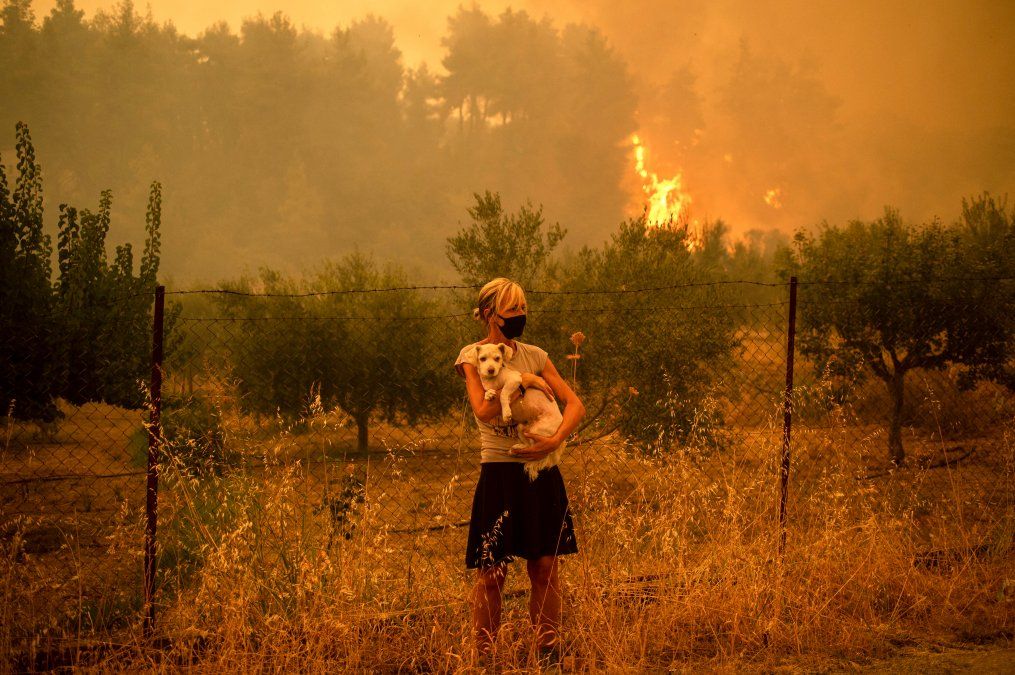 Una mujer sostiene un perro en sus brazos mientras los incendios forestales se acercan a la aldea de Pefki en la isla de Eubea