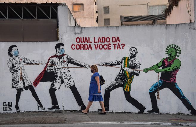 En esta foto de archivo tomada el 12 de junio de 2020, una mujer pasa junto a un mural que representa al presidente brasileño Jair Bolsonaro y una figura que representa al nuevo coronavirus COVID-19 tirando de una cuerda contra los trabajadores de la salud con la pregunta ¿De qué lado de la cuerda estás? En Sao Paulo, Brasil, se confirmó el tercer caso de la nueva variante COVID-19, omicron, en un viajero proveniente de Etiopía