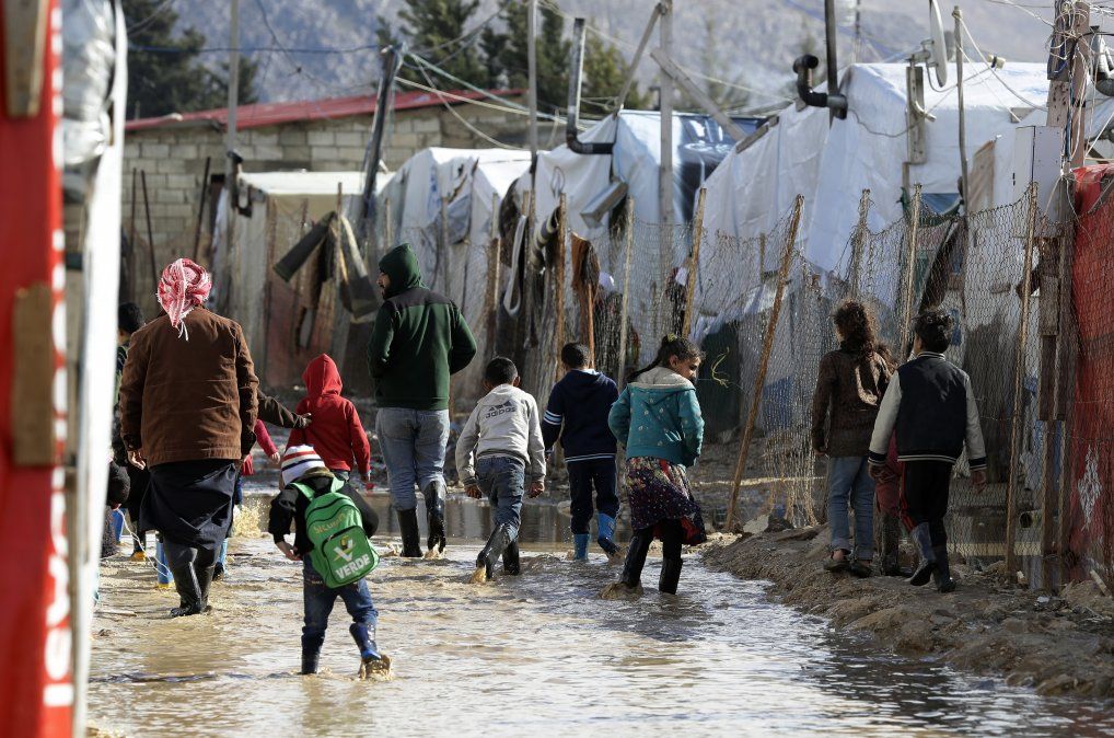 Refugiados caminan sobre zonas inundadas y cubiertas de barro en un campamento de sirios tras las tormentas de invierno. 