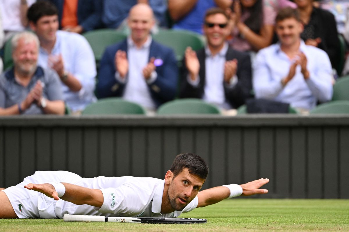 El serbio Novak Djokovic se acuesta en el césped durante su partido de tenis individual masculino de cuartos de final contra el italiano Jannik Sinner, en el noveno día del Campeonato de Wimbledon 2022 en el All England Tennis Club en Wimbledon, suroeste de Londres, el 5 de julio de 2022.