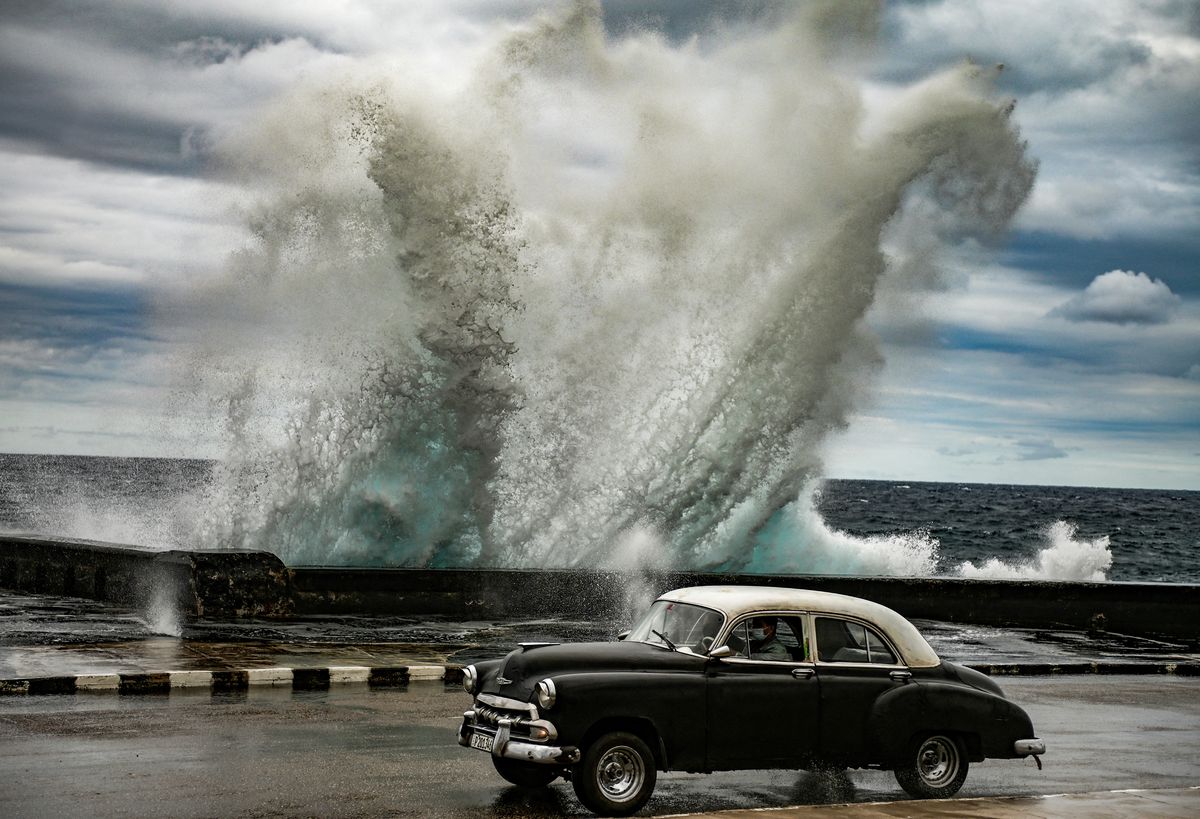 Un viejo automóvilestadounidense pasa por una zona donde un fuerte viento empuja unaola en el Malecón de La Habana.