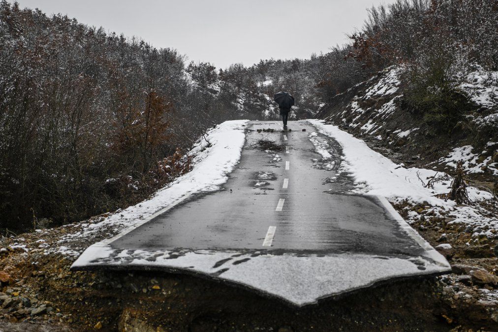 Un hombre pasa junto a una carretera colapsada debido a las fuertes inundaciones en la aldea de Sferke.