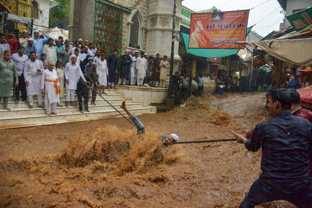 Un hombre cae a aguas de la inundación mietntras trata de agarrarse a una cuerda para ayudar a personas a cruzar la calle tras las fuertes lluvias del monzón, en Rajastán, India