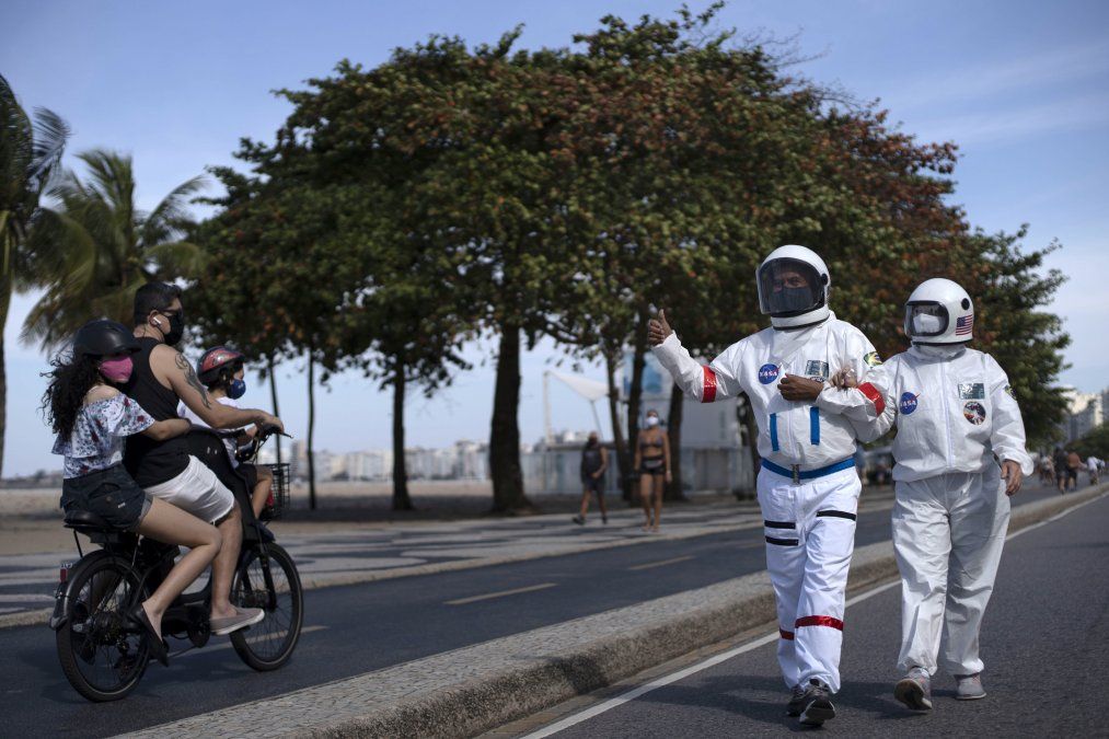 Una pareja de brasile&ntilde;os camina por Copacabana con trajes de astronauta para evitar contagiarse de coronavirus
