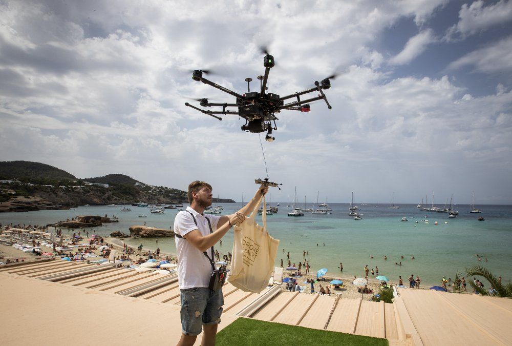 Un piloto de drones amarra una bolsa de comida a un dron en Cala Tadira. Drone to Yacht es un servicio de entrega exclusivo para la entrega de alimentos y bebidas a los yates.