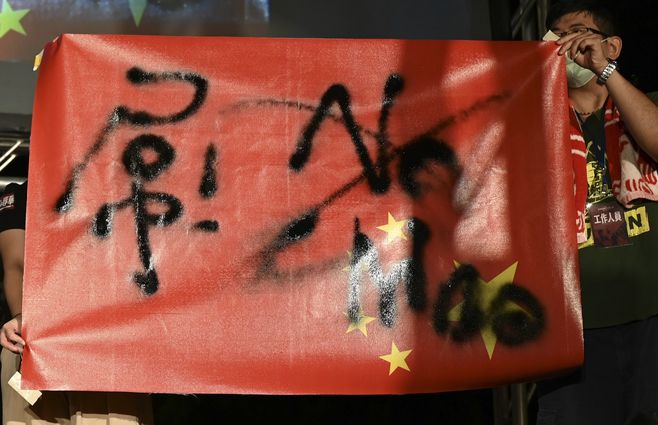 Manifestantes taiwaneses sostienen la bandera nacional de China al revés con escritos sobre ella durante una manifestación contra China frente al parlamento en Taipei.