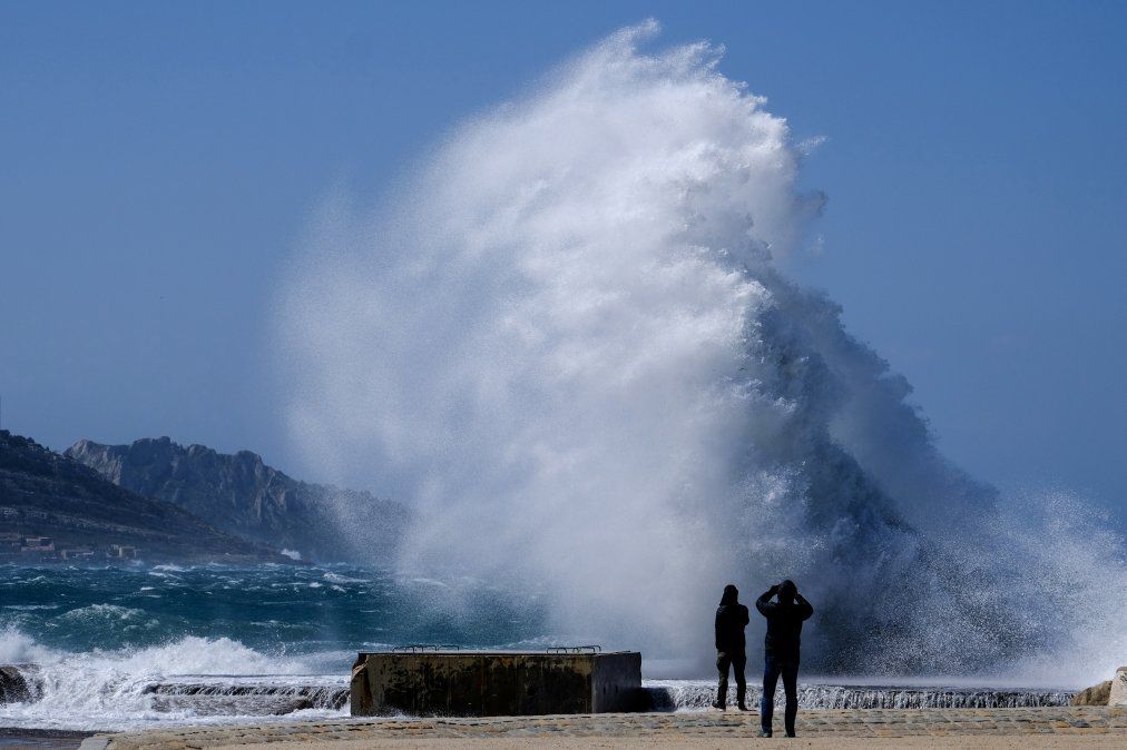 Personas miran las fuertes olas golpeando la orilla en la Playa de David en Marsella