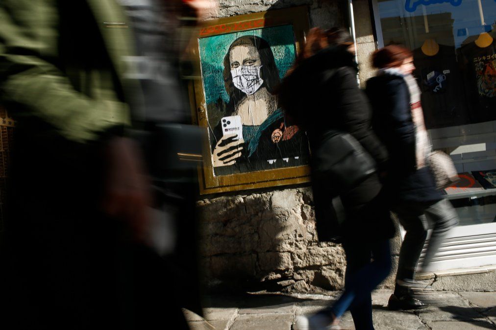 La gente camina cerca de un poster de un artista urbano italiano Salvatore Benintende que retrata a la Mona Lisa de Leonardo Da Vinci usando un tapabocas.