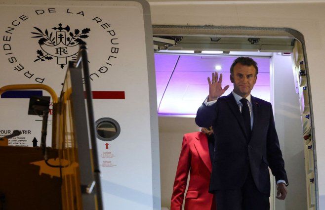 Macron al bajar del avión junto a su esposa, en ese momento detrás, luego al costado. Foto: AFP