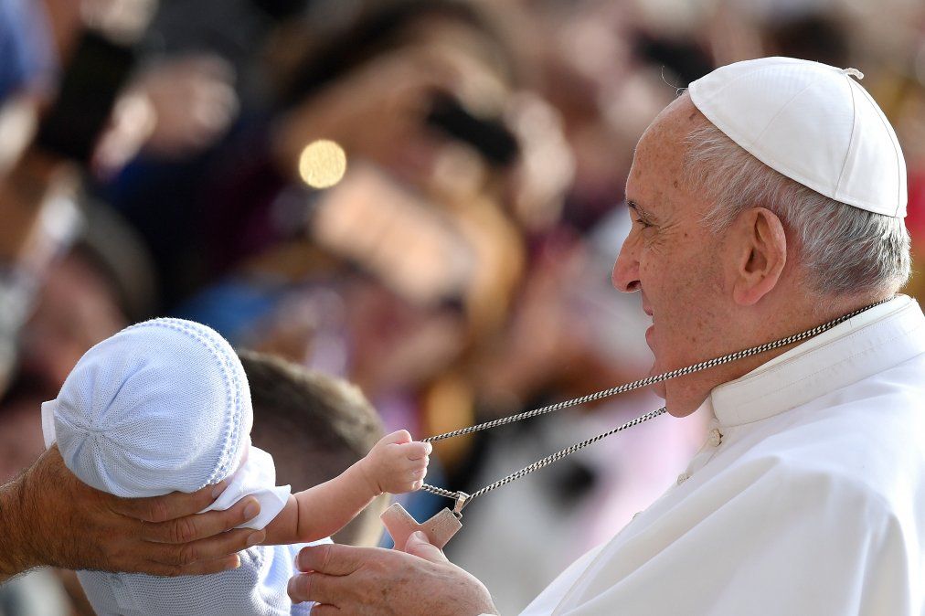 Un niño tira de la cadena que cuelga alrededor del cuello del Papa Francisco mientras saluda a los fieles