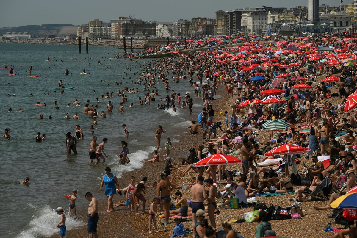 Los bañistas se sientan al sol en la playa y reman en el mar en Brighton, sur de Inglaterra, el 17 de julio de 2022. Foto: AFP