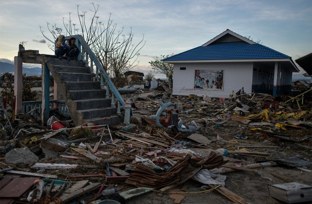 Dos mujeres se sientan en una dañada escalera de una escuela destruída por el tsunami en Palu, Indonesia.